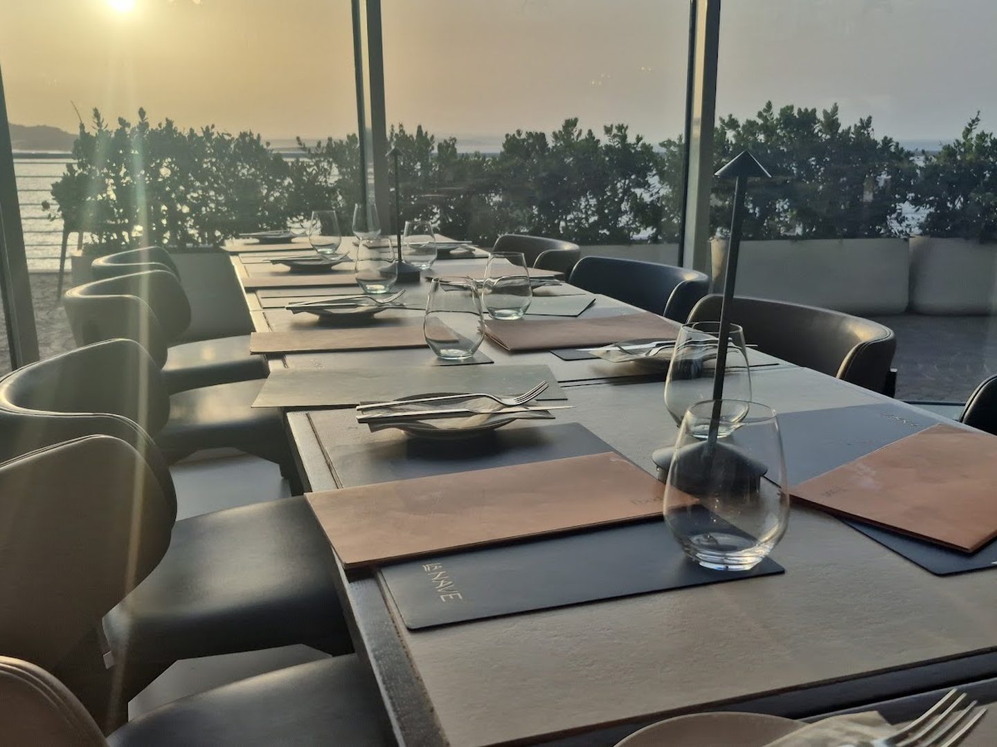 Dining room with laid tables, tall windows and planting along the glass