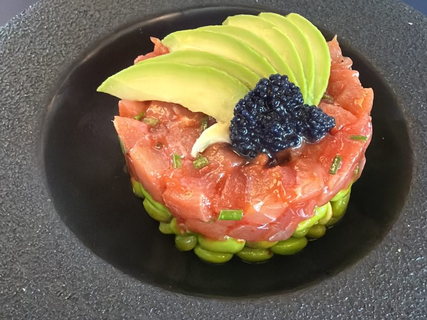 Salmon tartare ring with avocado fan and caviar on a dark plate