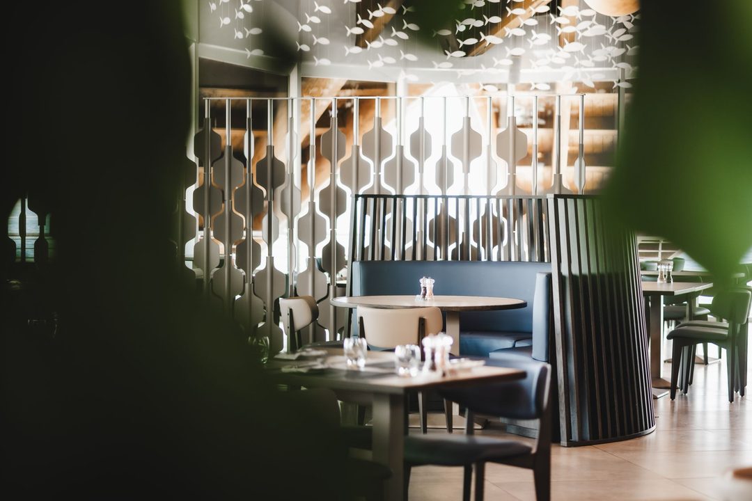 The dining room at La Nave, with a hanging shoal of paper fish above wave patterned screens and blue banquette seating