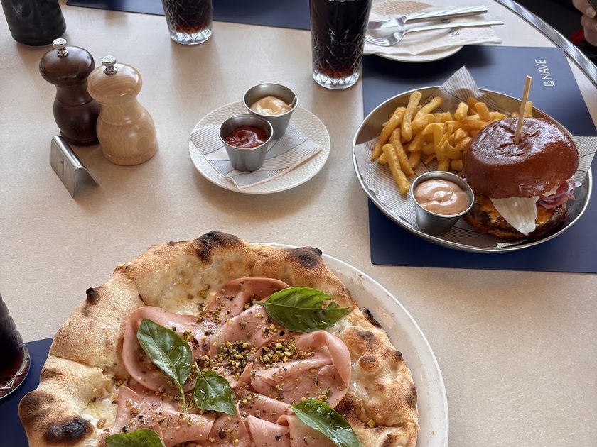 Pizza topped with cured ham and rocket, with fries and drinks alongside