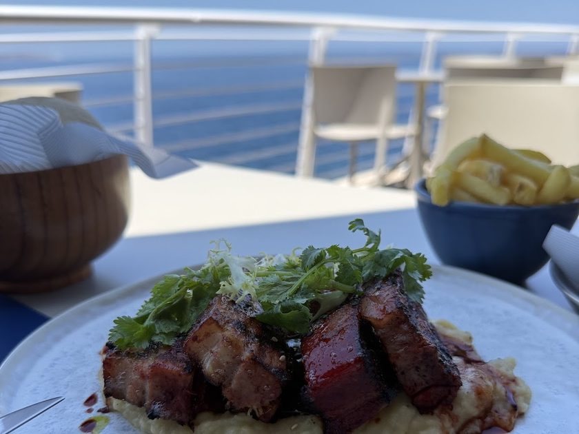 Sliced steak with herb dressing and greens on a blue table with the sea behind