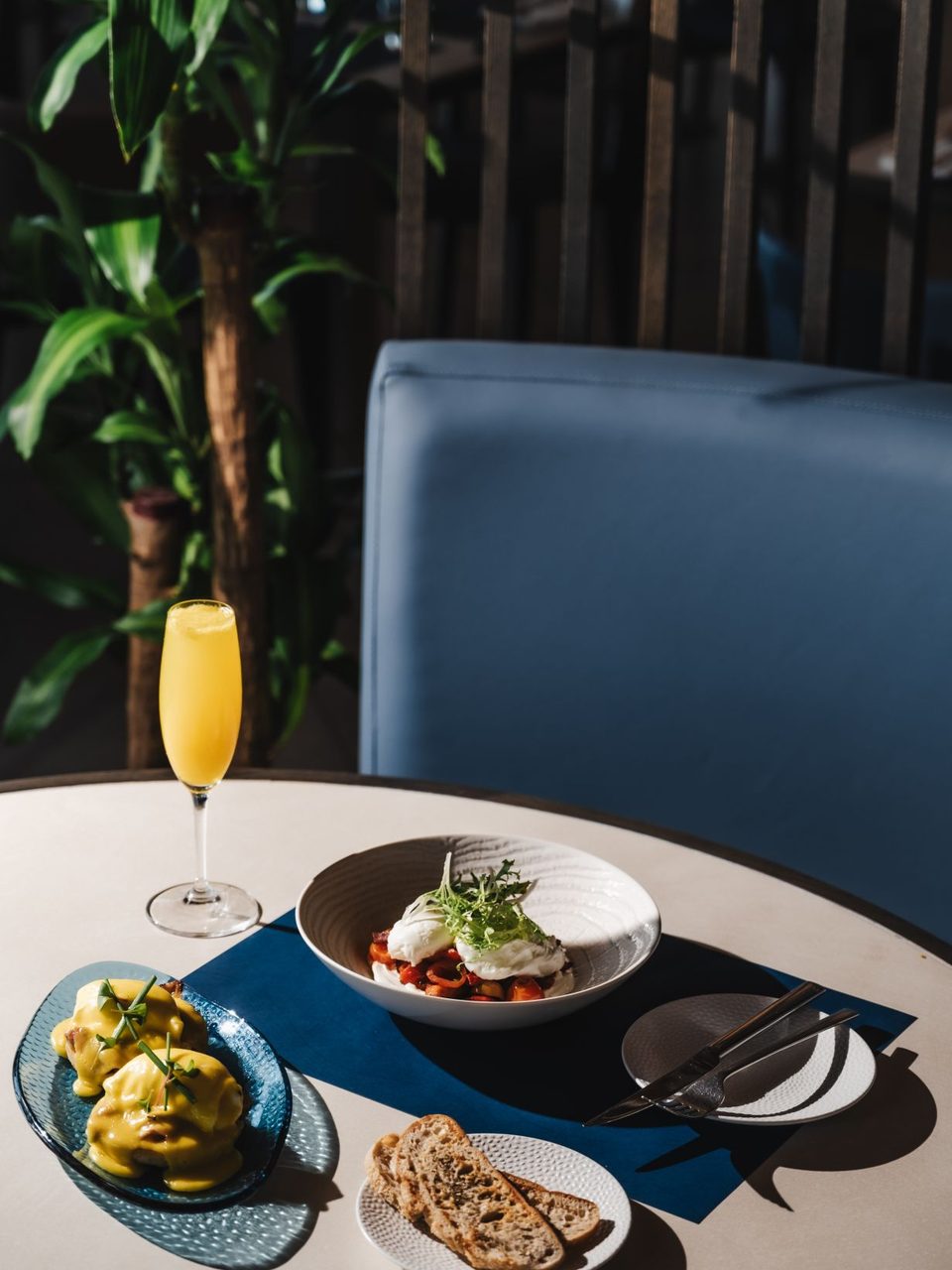 Breakfast on a round table with eggs benedict, poached eggs, sourdough toast and a glass of orange juice